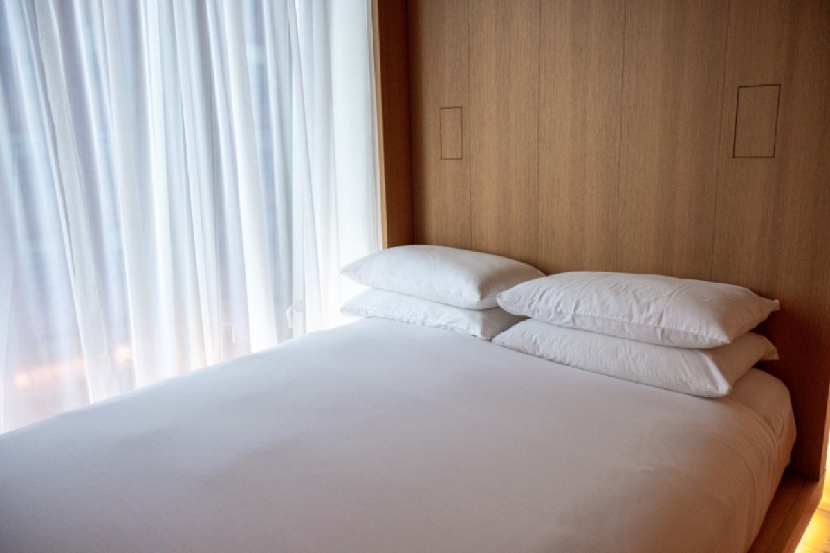 Opgemaakt bed met witte kussens en dekbed voor een raam met vitrage