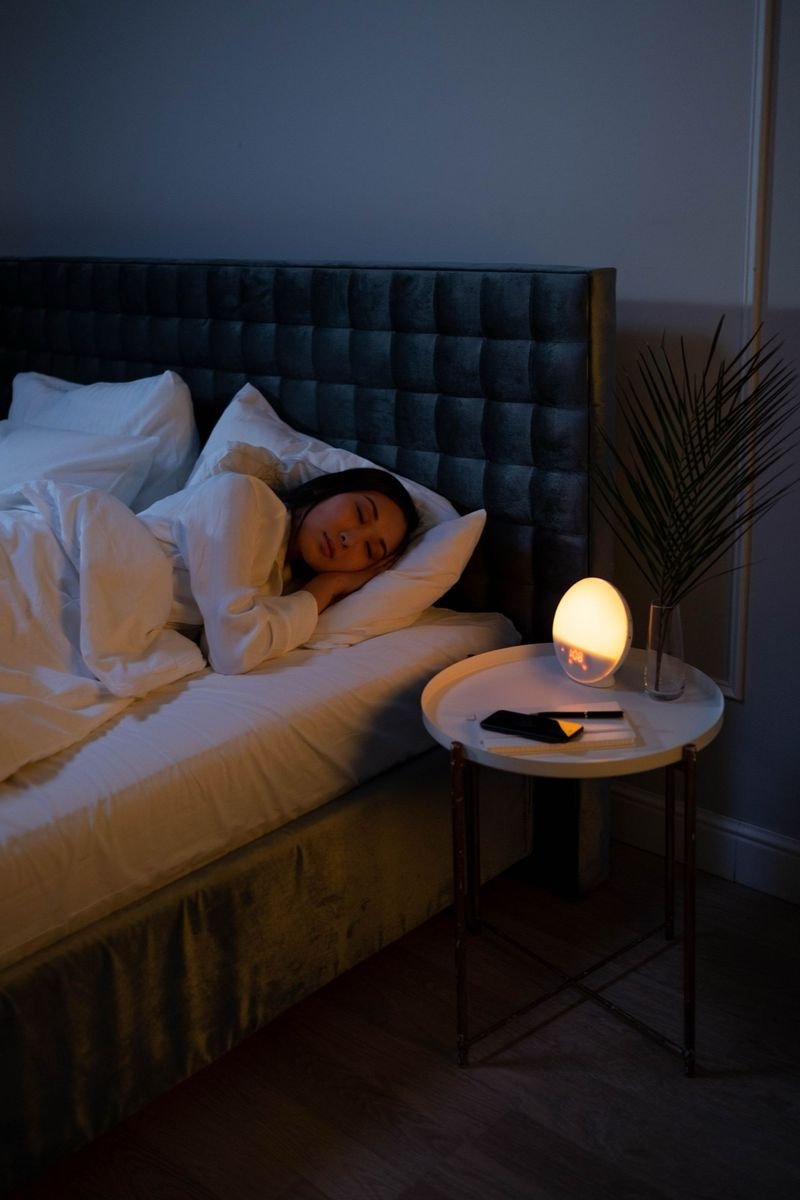 Vrouw slaapt op haar zij met haar hoofd op een wit kussen, naast een nachtkastje met lamp